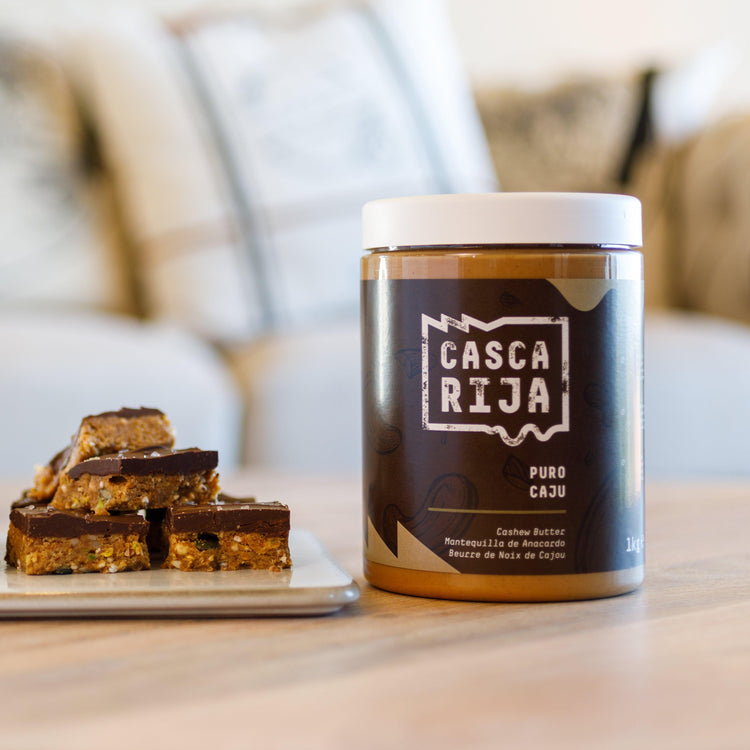 Frasco de manteiga de caju 1 kg ao lado de quadrados de sobremesa